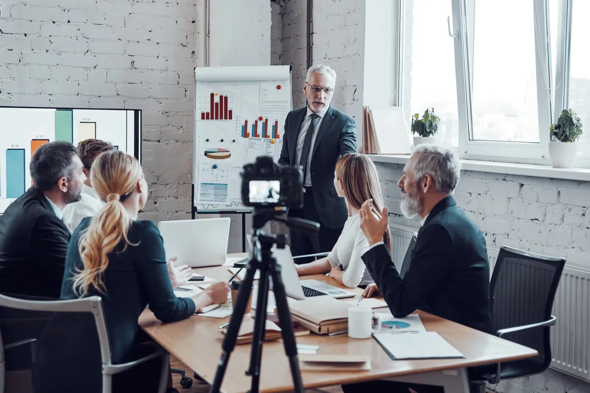 Successful business team listen a man which conducting presentation while filming staff meeting in the board room
